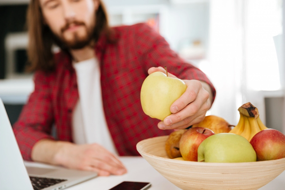 Primer plano de un hombre comiendo fruta y usando el portátil en el trabajo