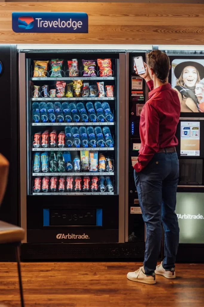 Hombre usando su teléfono móvil para pagar en una máquina expendedora de bebidas y snacks en un hotel.